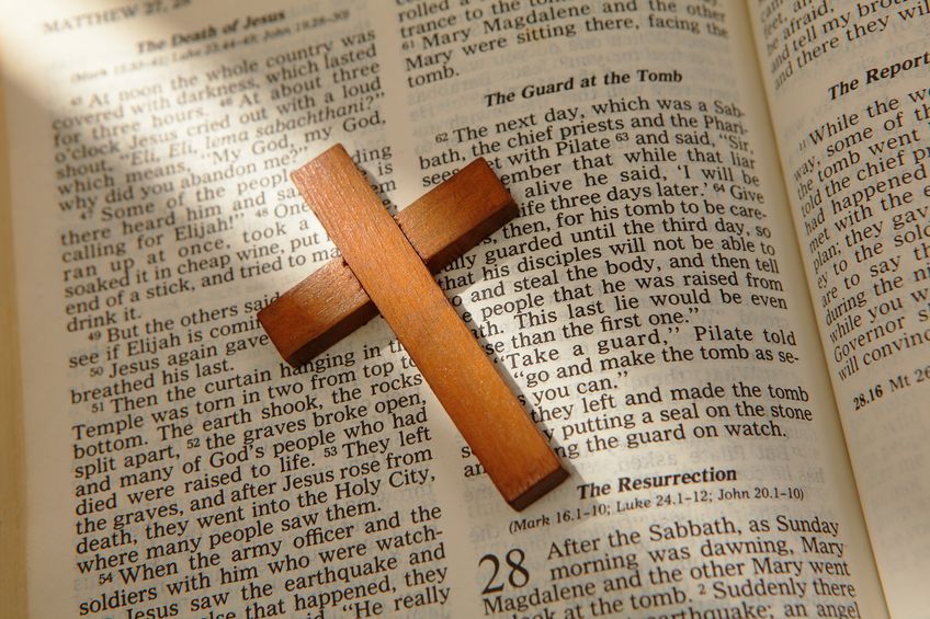 Wooden cross on an open Bible showing the resurrection and empty tomb